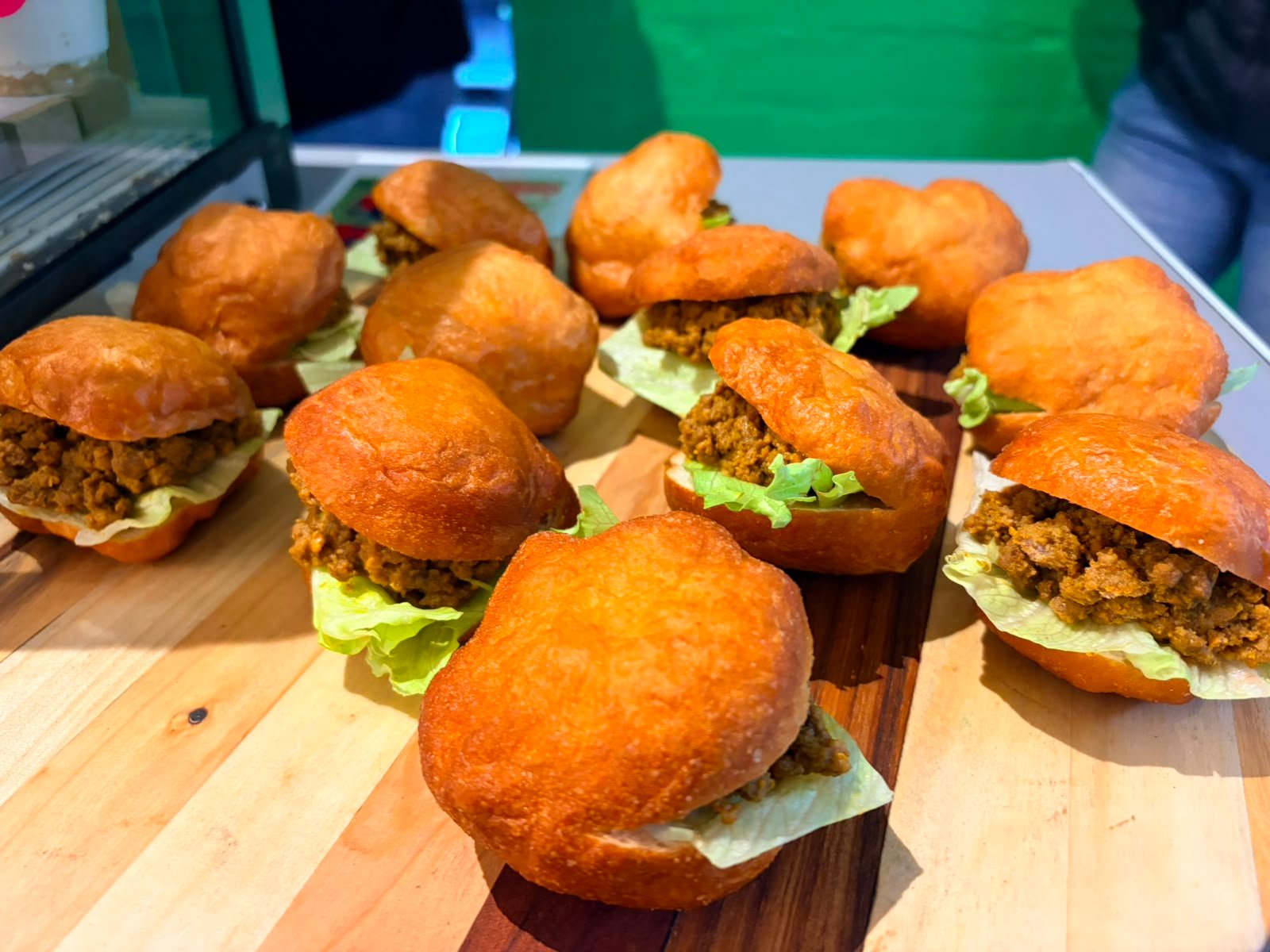 Vetkoek filled with curried mince and lettuce, lined up on a wooden board